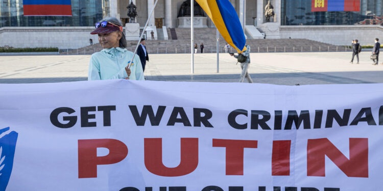 A woman holding a Ukranian national flags and a banner takes part in a protest ahead of a visit by Russian President Vladimir Putin in Ulaanbaatar, Mongolia's capital city on September 2, 2024. (Photo by Byambasuren BYAMBA-OCHIR / AFP)